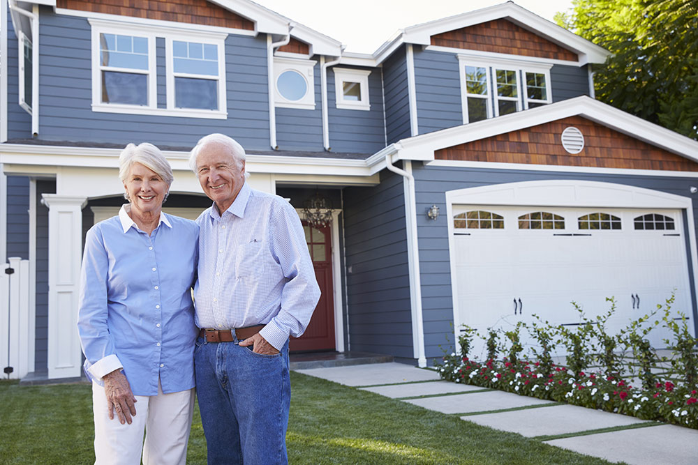 Senior man and woman standing out in front of a blue house with white trim
